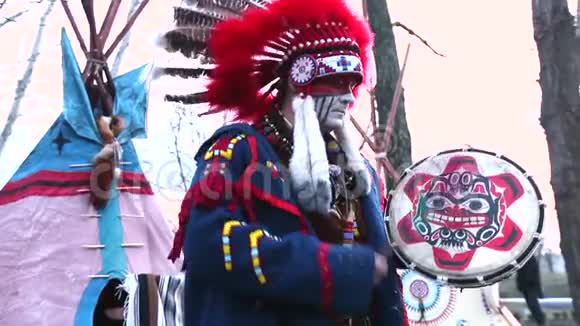 穿着全套衣服的北美印第安人一个穿着西装的印第安人在wigwam前面的街道上和一只手鼓跳舞视频的预览图