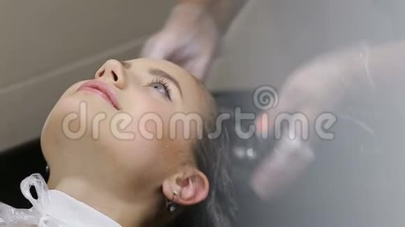 戴手套的理发师给年轻女人洗发廊里的头发视频的预览图