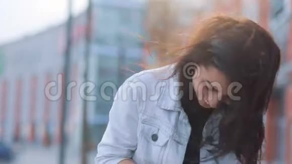 年轻迷人的棕色头发和棕色眼睛的女孩穿着白色牛仔裤外套和黑色T恤通过智能手机在附近通勤视频的预览图