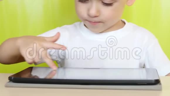 坐在桌子旁的小男孩摸着平板电脑的电子显示器一个孩子在玩手提电脑视频的预览图