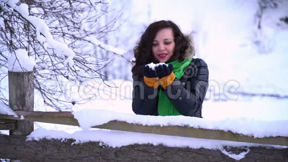 一个下雪公园里的年轻漂亮女孩她站在木栅栏附近女孩手里拿着雪吹着视频的预览图