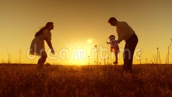 一个小孩子学会和爸爸妈妈一起散步年轻漂亮的家庭在夕阳下和孩子一起在田野里散步慢动作视频的预览图