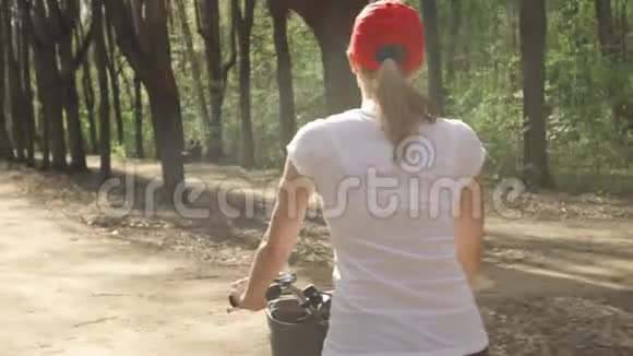 快乐活泼活泼的年轻女子在夏日阳光明媚的公园里骑着红帽子自行车视频的预览图