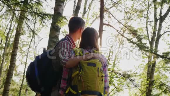 一对年轻的游客在日落时在树林里散步他们站着拥抱向前看背面视频的预览图