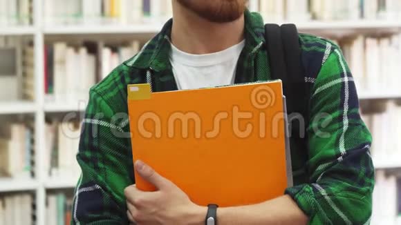 一个手里拿着课本的年轻学生正站在图书馆里视频的预览图
