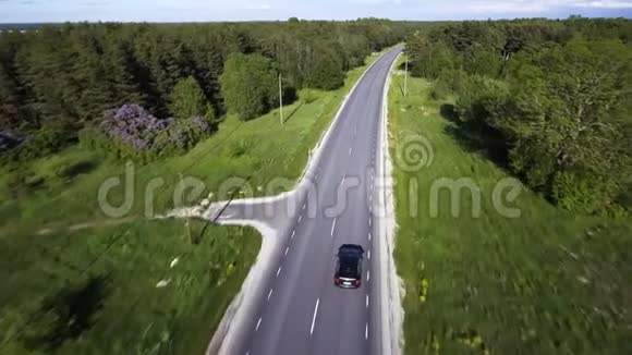 两车道森林公路的鸟瞰图一辆黑色汽车在两边茂密森林中的绿树之间行驶视频的预览图