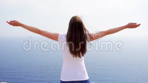 女人举起手臂在悬崖上对着蓝色的大海女性劳动者伸出双手视频的预览图