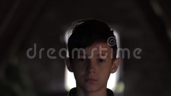 一个严肃悲伤的男孩在黑暗的房间里看着摄像机脸上疼痛视频的预览图
