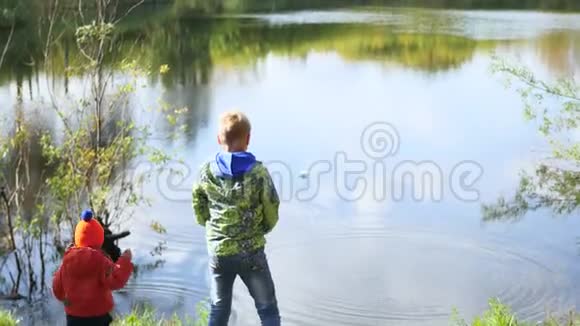 孩子们站在池塘的岸边扔石头在新鲜空气中游走视频的预览图