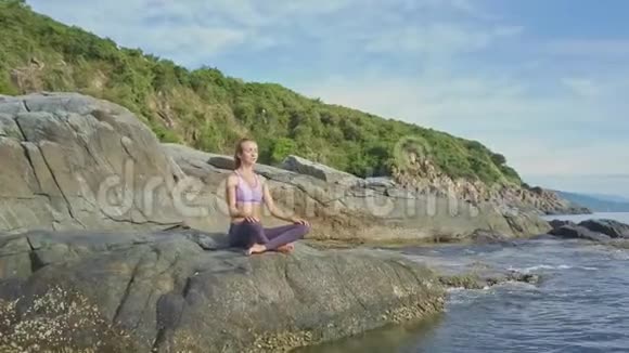 女孩专注于瑜伽姿势在岩石海滩对抗波浪视频的预览图
