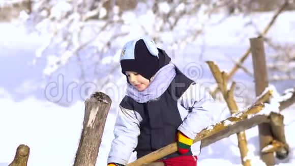 冬天公园里漂亮的小男孩他坐在木栅栏上玩棍子视频的预览图