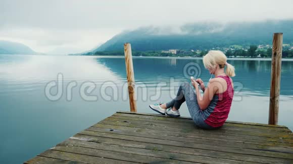 总是联系在一起一位女士使用智能手机坐在阿尔卑斯山一个风景如画的湖边视频的预览图