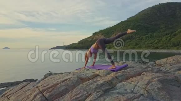 金发女孩在岩石海洋海滩做瑜伽姿势视频的预览图