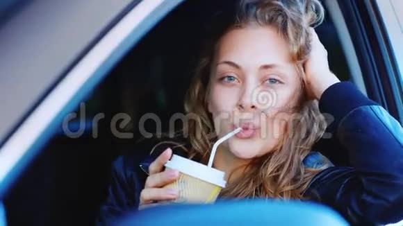 一位年轻独立女性在车上的肖像坐在方向盘上看着摄像机拿着一杯咖啡视频的预览图