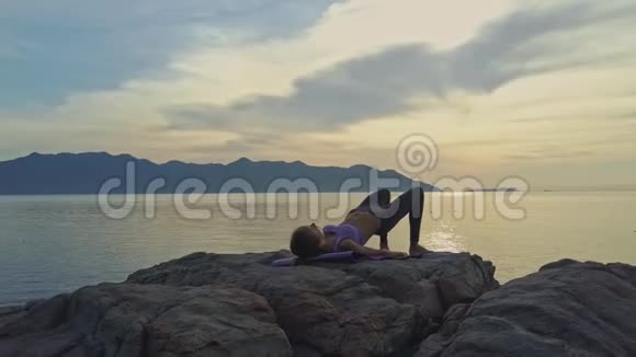 女孩做瑜伽练习躺在岩石上对抗海洋视频的预览图