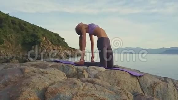 日出时带马尾辫的女孩在海边的山上做瑜伽视频的预览图