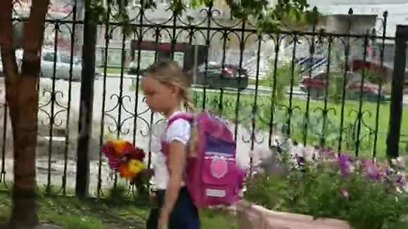 女孩沿着铁栅栏快速行走带着背包和鲜花去学校回到学校的概念金发少女视频的预览图