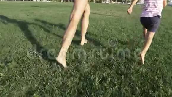 在公园的草地上奔跑的妈妈和小女儿的特写双脚视频的预览图