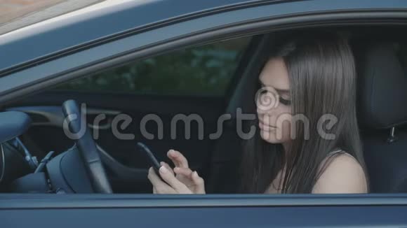 年轻漂亮的女人坐在车里用智能手机视频的预览图