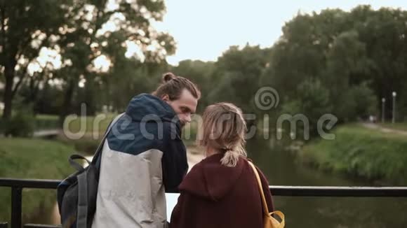 日落时在公园里散步的年轻漂亮夫妇时髦的男人和女人站在桥上说话视频的预览图