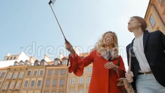 两位年轻的女游客正在镇上用自拍棒打电话视频的预览图