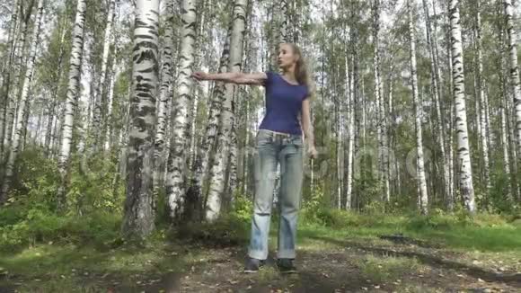 这位身材苗条的年轻女子穿着t恤和牛仔裤留着一头细密的长发在林中空地上与武术搏斗视频的预览图