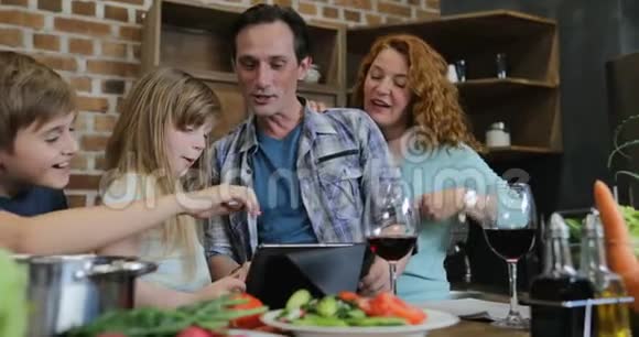 家庭幸福在厨房里使用数字平板触摸屏做饭父母带着两个孩子在家聊天视频的预览图