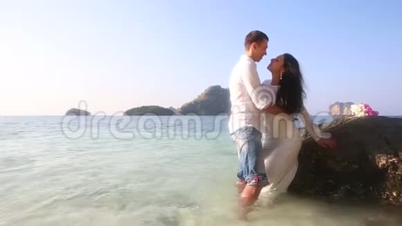 新娘和新郎靠在岩石上站在海里视频的预览图