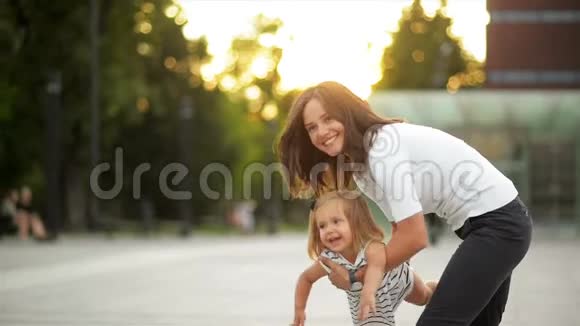 美丽年轻的母亲托起女儿在城市广场日落时在户外玩耍快乐的小女孩视频的预览图
