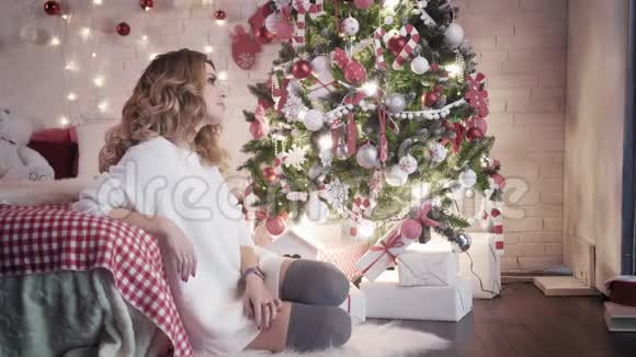 一个年轻人送给一个坐在圣诞树附近的漂亮年轻女人一份圣诞礼物他们一起微笑视频的预览图