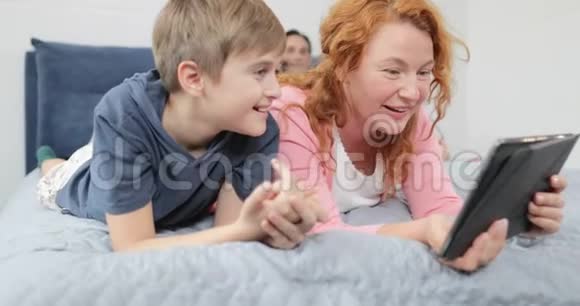 幸福的母亲和儿子把平板电脑躺在卧室里家庭一起度过时光视频的预览图