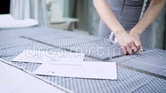 年轻的女设计师站在裁剪工作室的桌子旁用粉笔和规则在布上做线条视频的预览图