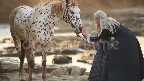 马疗法河马疗法穿着经典服装的女人站在海岸上与小女儿和斑驳的马结合在一起视频的预览图