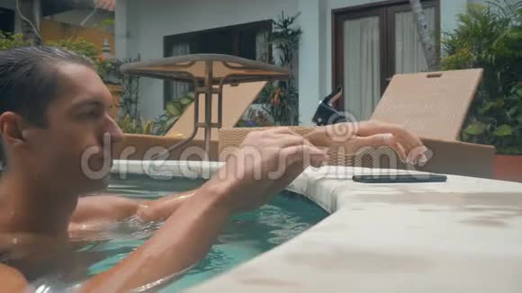 年轻人在游泳池里游泳在暑假用智能手机聊天视频的预览图
