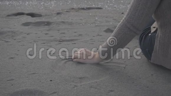 一个女孩在沙滩上捡沙子并让沙子掉下来的慢镜头视频的预览图