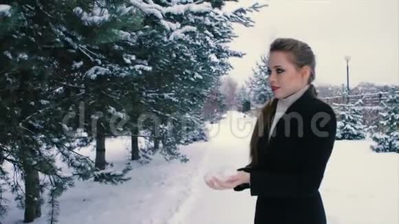 布鲁内特女士在户外的松树冬季公园里扔雪慢动作视频的预览图