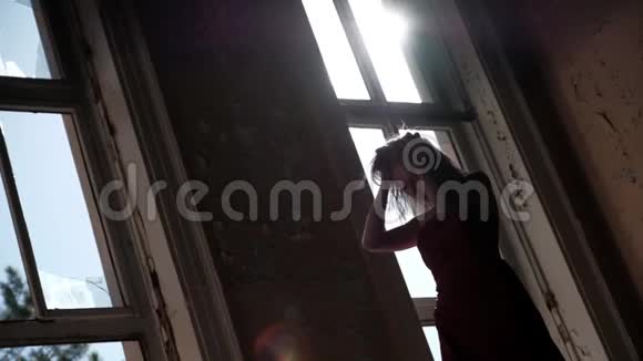 一个穿着红色长裙的年轻女子站在一座废弃的房子里站在灯光下表情迷人地抚摸着她的头发视频的预览图