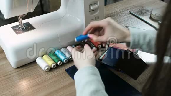 裁缝在桌子上拿起一根线对织物和皮革背景中的缝纫机视频的预览图