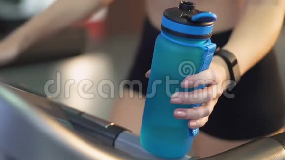 年轻女士在健身房跑步机上行走手里拿着水瓶水平衡视频的预览图