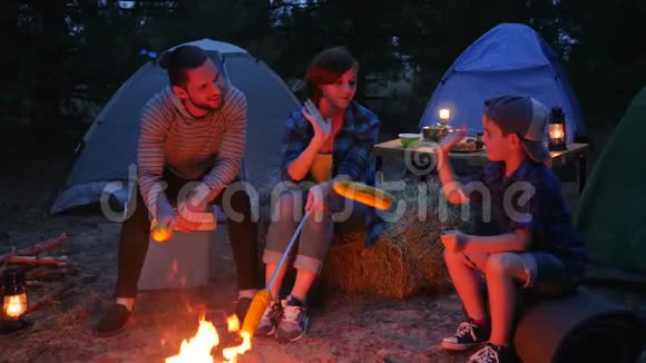 妈妈儿子和爸爸用串串的烤玉米带着帐篷旅行在森林野餐美国家庭围着视频的预览图