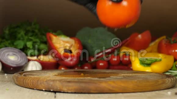 黑色手套的厨师将多汁的红番茄与水滴的特写放在背景上的木板上视频的预览图