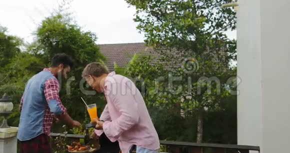 两个男人在烧烤上放食物年轻的朋友小组在夏天的露台上聚会快乐跳舞视频的预览图