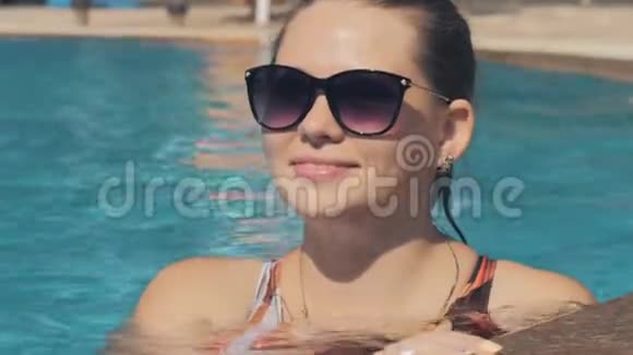 一个美丽的白种人女人的肖像是一个游泳池美丽的长发女孩在蓝色的游泳池里放松视频的预览图