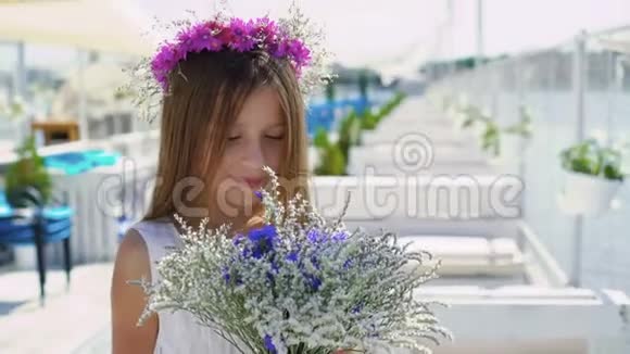 快乐的小女孩闻着花看着海湾酒吧的相机4K视频的预览图