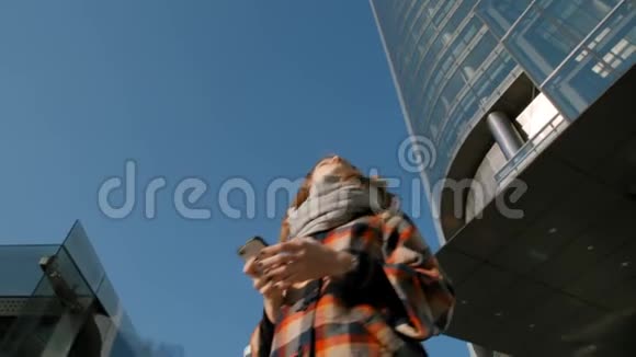 女人在摩天大楼的背景下环顾四周拿着智能手机视频的预览图