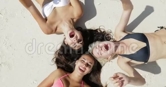 俯瞰三个女孩躺在沙滩上欢笑享受阳光晒晒的谈话女人在暑假快乐的游客视频的预览图