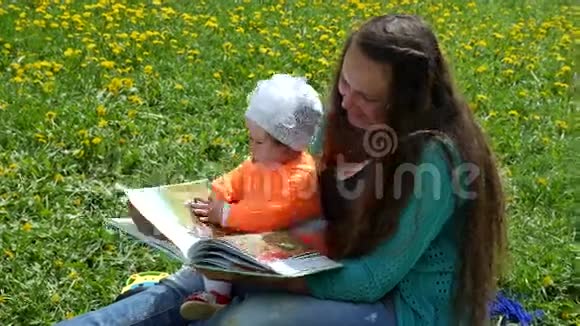 一个快乐的孩子和他的家人在蒲公英的春天的小路上坐在母亲腿上读一本书视频的预览图