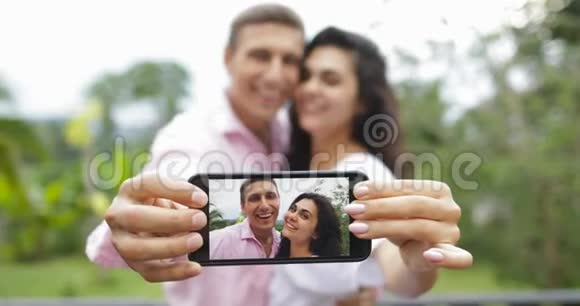 情侣手持手机拍照拥抱热带森林的亲吻户外年轻人和女人视频的预览图