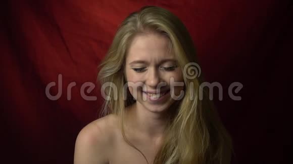 一个可爱的金发女郎站在暗红色背景上笑着慢动作视频的预览图