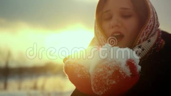 一位美丽的年轻女子在日落时分用镜头轻轻地吹着雪花微笑着视频的预览图